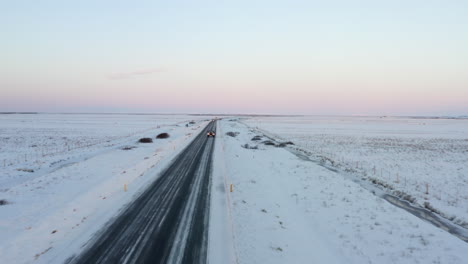 Antena:-Primer-Plano-De-Las-Luces-De-Freno-Del-Jeep-Conduciendo-Por-La-Carretera-De-Islandia-Con-Montañas-Blancas-Como-La-Nieve-Y-Nieve-Al-Atardecer,-ártico
