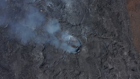 Aerial-birds-eye-overhead-top-down-view-of-Fagradalsfjall-volcano-smoking-crater-fissure-hole,-drone-rising-up-reveal-black-lava-landscape,-Iceland,-day