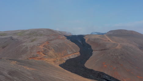 Antena-Dando-Vueltas-Alrededor-Del-Río-De-Lava-Negra-Que-Fluye-Entre-Montañas-En-Fagradalsfjall,-Islandia,-Día