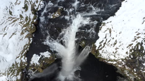 AERIAL:-Close-Up-of-Waterfall-in-Snow,-Ice-Canyon-in-Iceland-flying-upwards-Green-Grass,-Cloudy