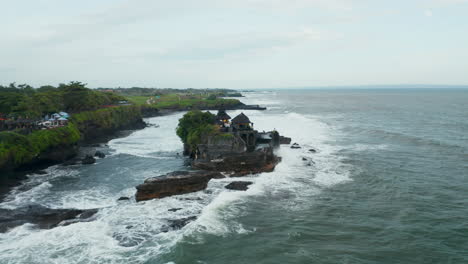 Wide-aerial-dolly-shot-of-isolated-empty-Tanah-Lot-temple-during-dangerous-weather.-Strong-waves-crashing-into-dark-rocky-cliff-with-famous-Hindu-temple-in-Bali,-Indonesia