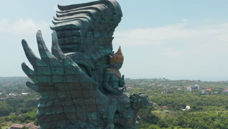 Side-dolly-aerial-view-of-giant-Garuda-Wisnu-Kencana-statue-in-Bali,-Indonesia.-Statue-of-Garuda-being-ridden-by-Vishnu-rising-above-the-town