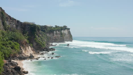 Wild-steep-rocky-cliffs-and-blue-ocean-in-Bali,-Indonesia.-Aerial-dolly-shot-of-waves-crashing-in-stunning-rocky-ocean-coastline-in-Bali