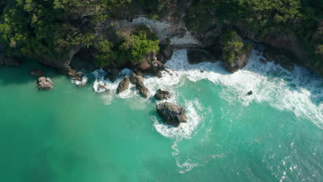 Blue-waves-crashing-on-the-tropical-coastline.-Aerial-tilting-view-of-turquoise-blue-water-foaming-around-the-rocky-cliffs