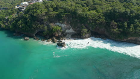 Wilde-Ozeanwellen,-Die-Auf-Felsklippen-An-Der-Tropischen-Bali-küste-Krachen.-Luftaufnahme-Von-Türkisblauem-Wasser,-Das-Um-Die-Felsigen-Klippen-Spritzt
