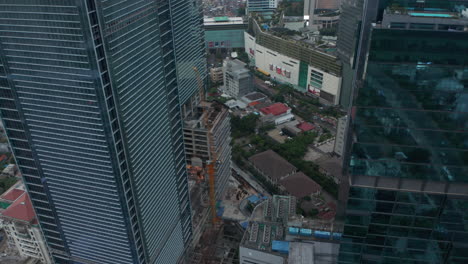 Aerial-dolly-shot-flying-between-skyscrapers-towards-small-green-residential-neighborhood-in-the-city-of-Jakarta,-Indonesia