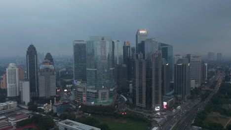 Aerial-truck-view-circling-around-a-building-complex-of-multiple-skyscrapers-in-modern-city-center-by-a-motorway-in-Jakarta