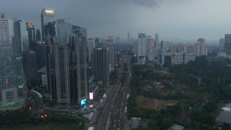 Aerial-dolly-view-following-traffic-on-a-busy-motorway-in-the-evening-surrounded-by-tall-skyscrapers-and-athletic-field-in-Jakarta