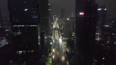 Aerial-dolly-shot-of-a-single-police-car-driving-down-an-empty-multi-lane-highway-at-night-surrounded-by-tall-skyscrapers-in-city-center-of-Jakarta