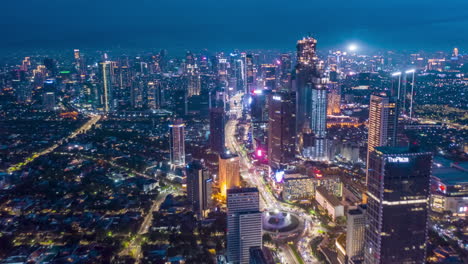 Stunning-City-View-of-Futuristic-Skyline-at-Night,-Skyscrapers-in-Asian-Indonesian-Capital-Jakarta-with-flashing-lights-and-Car-Traffic-Flow-on-Main-road,-Aerial-Hyperlapse-Time-Lapse,-Drone-View