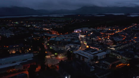 Aerial-panoramic-shot-of-evening-town-and-lake-surrounded-with-mountains-in-background.-Killarney,-Ireland