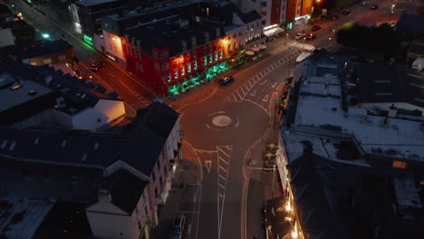 Fly-above-illuminated-street-in-city.-Colourful-house-facades-along-road-in-town-centre-at-night.-Killarney,-Ireland