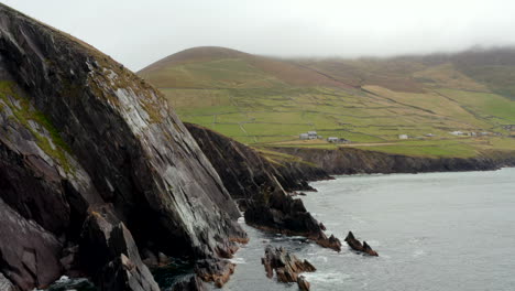 Jagged-coastal-rocks-and-tall-steep-cliffs-along-sea-coast.-Countryside-with-green-meadows-and-pastures.-Ireland