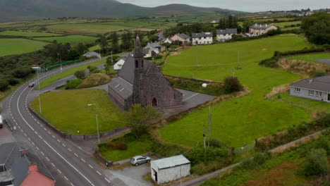Pull-back-footage-of-old-stone-church-standing-at-road-in-village-in-countryside.-Overcast-sky.-Ireland