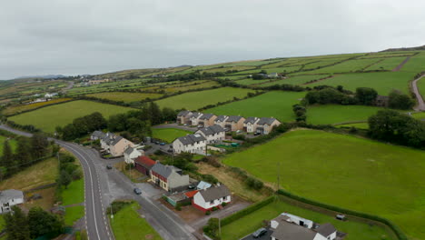 Slide-and-pan-aerial-shot-of-group-of-family-houses-in-village.-Green-meadows-and-grasslands-in-slope-behind.-Ireland