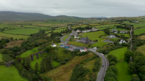 High-angle-view-of-road-winding-through-village-with-sparse-housing-development.-Tilt-up-reveal-of-countryside-panorama.-Ireland