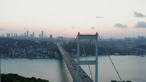Istanbul-15-July-Martyrs-Bosphorus-Bridge-and-City-Skyline-in-Background-with-Turkish-Flag-at-Beautiful-Sunset,-Aerial-slide-right