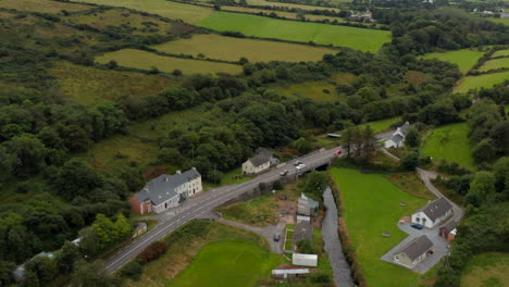 Aerial-view-of-road-leading-around-houses-in-village-in-valley.-Tilt-up-reveal-of-countryside-panorama-with-green-fields-and-meadows.-Ireland