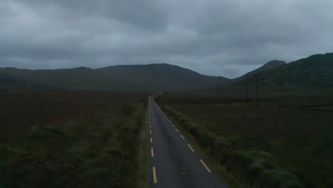 Narrow-road-with-dashed-lines-marked-edges-in-landscape-at-dusk.-Fly-against-car-arriving-from-distance.--Ireland
