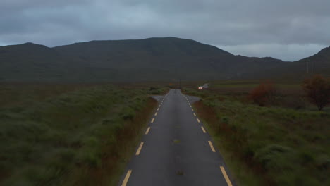 Low-flight-above-narrow-road-in-countryside.-Ascending-and-revealing-oncoming-offroad-car-with-trailer.-Mountain-ridge-in-background.-Ireland