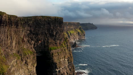 Forwards-fly-along-amazing-scenic-cliffs.-High-vertical-rock-walls-falling-into-rippled-water.-Cloudy-sky.-Cliffs-of-Moher,-Ireland