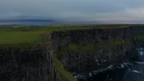 Tilt-up-reveal-on-high-rock-cliffs-above-sea-surface.-Waves-rolling-to-coast.-Natural-scenery-at-twilight.-Cliffs-of-Moher,-Ireland