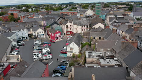Fly-above-houses-in-urban-borough.-Square-with-parked-cars-around-and-in-middle.-Tilt-up-reveal-of-overcast-sky.-Ennis,-Ireland