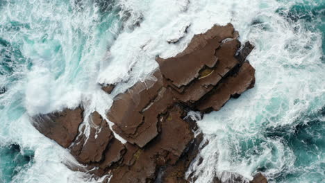 Aerial-birds-eye-overhead-top-down-descending-and-rotating-view-of-waves-crashing-and-rolling-over-coastal-rocks.-Abstract-natural-scenery.-Kilkee-Cliff-Walk,-Ireland