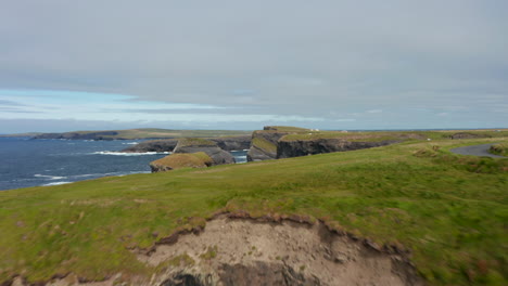 Fly-along-high-cliffs.-Vertical-rock-walls-above-rippled-sea-surface.-Beautiful-landscape-scenery.-Kilkee-Cliff-Walk,-Ireland