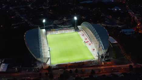 Aerial-view-of-football-stadium-glowing-into-night.-Bright-lights-illuminating-green-playground.-Limerick,-Ireland