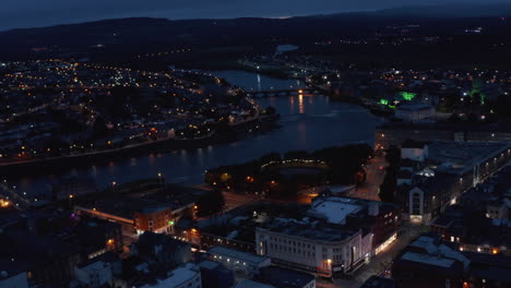 Fly-above-city-in-evening.-Aerial-view-of-river-flowing-through-night-town-with-street-lights.-Limerick,-Ireland