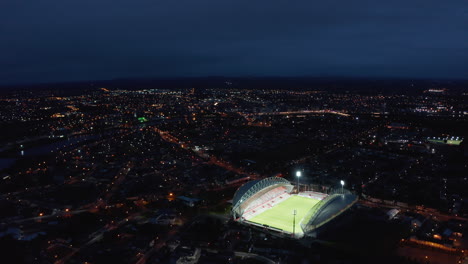 Luftpanoramablick-Auf-Die-Nachtstadt.-Helle-Lichter,-Die-Auf-Das-Grüne-Fußballspielfeld-Scheinen.-Limerick,-Irland