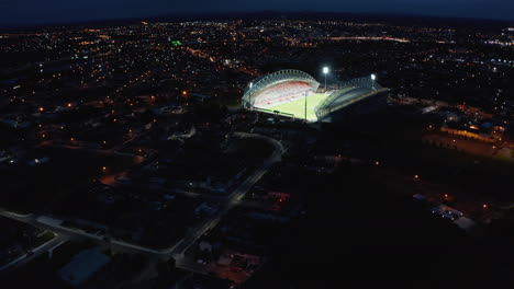 Descending-panoramic-footage-of-night-city-with-glowing-illuminated-football-stadium.-Limerick,-Ireland