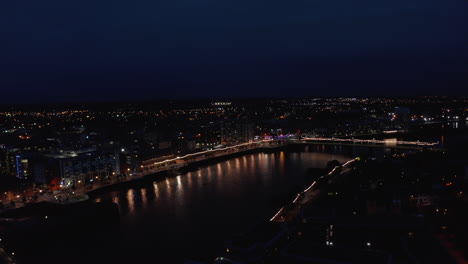 Aerial-panoramic-view-of-illuminated-bridge-and-waterfront-in-city.-Water-surface-reflecting-lights.-Shannon-river-calmly-flowing-in-night-town.-Limerick,-Ireland
