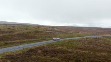 Tracking-of-single-vintage-convertible-car-with-textile-roof-driving-on-road-in-countryside-on-cloudy-day.-Ireland