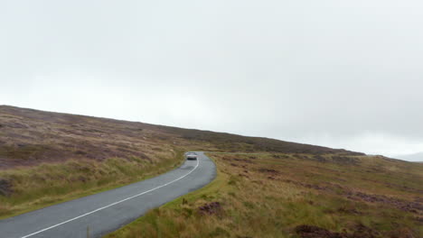 Forwards-tracking-convertible-car-on-wet-curvy-road-surrounded-by-meadows-and-grasslands-in-countryside.-Ireland