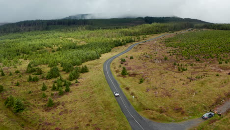 Panoramaaufnahmen-Aus-Der-Luft-Von-Autofahrten-Auf-Der-Straße-In-Hügeliger-Bewaldeter-Landschaft.-Hügelkuppen-In-Wolken-Im-Hintergrund.-Irland