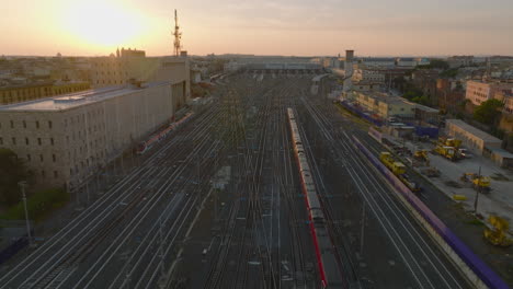 Forwards-tracking-of-passenger-train-unit-heading-to-central-train-station,-passing-by-next-train-moving-reverse-direction.-Aerial-view-against-sunset.-Rome,-Italy