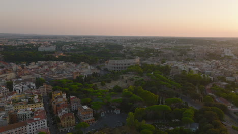 Aerial-slide-and-pan-footage-of-famous-ancient-Colosseum-amphitheatre-and-surrounding-parks-and-buildings-in-historic-city-centre-at-twilight.-Rome,-Italy