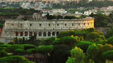 Aerial-slide-and-pan-footage-of-famous-and-popular-ancient-landmark.-Colosseum-in-sunset-time.-View-over-green-treetops-in-park.-Rome,-Italy