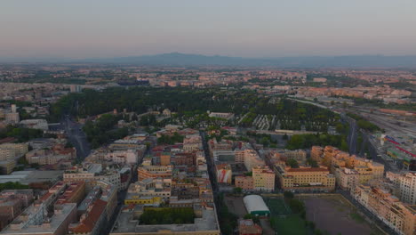 Aerial-slide-and-pan-footage-of-Tiburtino-urban-borough-with-large-cemetery.-Panoramic-view-of-city-at-dusk.-Rome,-Italy