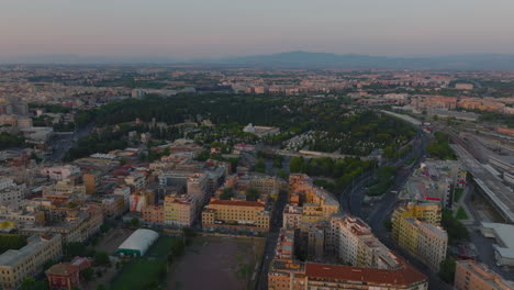 Panoramic-footage-of-large-city-at-twilight.-Aerial-view-of-Tiburtino-borough-with-cemetery.-Rome,-Italy
