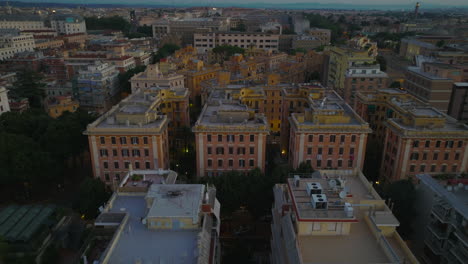 Backwards-fly-above-apartment-buildings-in-housing-estate-in-city.-Tilt-up-reveal-residential-urban-borough-at-twilight.-Rome,-Italy