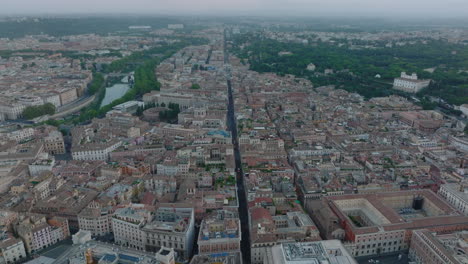 Aerial-descending-footage-long-straight-street-leading-through-historic-city-centre-of-metropolis-at-twilight.-Rome,-Italy