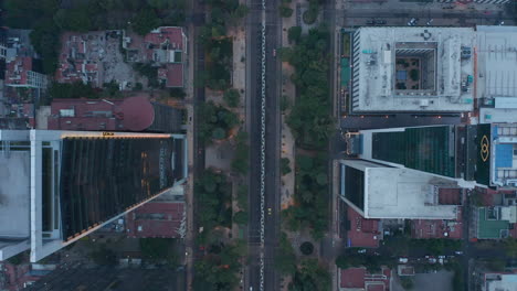 Top-down-view-of-cars-driving-on-road-and-tall-building-along-street-in-Mexico-city.-Drone-slowly-ascending-and-revealing-rooftops-of-further-building.