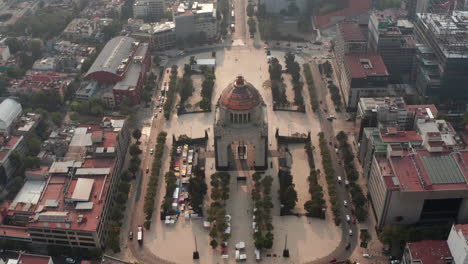 Aerial-view-from-drone-on-famous-Monument-to-Revolution-on-Plaza-de-la-Republica.-Camera-angle-tilting-up-to-city-panorama-against-sun.-Mexico-city,-Mexico.