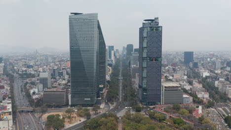 Drone-flying-forwards-from-Chapultepec-park-between-tall-modern-office-buildings-on-wide-Avenida-Paseo-de-la-Reforma-street.-Mexico-city,-Mexico.