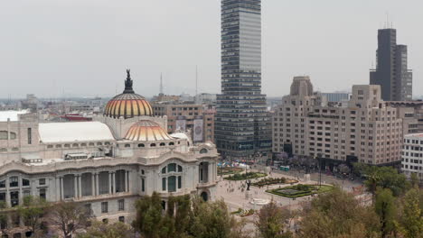 Reveal-of-city,-ascending-drone-flying-around-colourful-dome-with-bird-sculpture-of-Palace-of-fine-arts-(Palacio-de-Bellas-Artes)-in-historic-city.-Mexico-City,-Mexico.