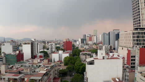 Rooftop-view-of-low-residential-houses-neighbors-with-tall-office-buildings.-Low-forward-flying-drone-camera-over-city-downtown.-Mexico-city,-Mexico.