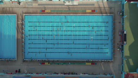 Nadadores-Entrenando-Dando-Vueltas-En-La-Piscina-Azul,-Perspectiva-épica-De-Pájaro-Bajo-El-Sol,-9-De-Septiembre-De-2020